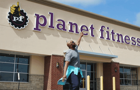 Man spins happily in front of Planet Fitness. 