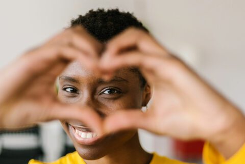 Woman’s hands make a heart shape in front of her face. 