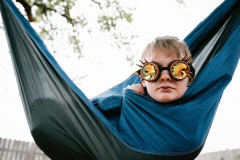 Little boy sits in hammock with quirky sunglasses on. 