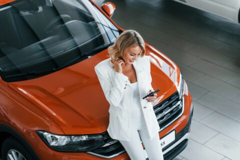 Woman in formal clothes leaning on orange car.
