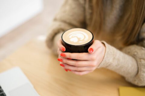 A pair of hands with red fingernail polish grasping a coffee cup.