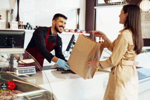 a man hands a woman a shopping bag in a luxury grocery store